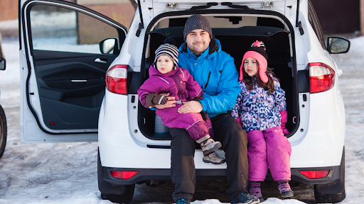 father and two kids sit in the back hatch of their car