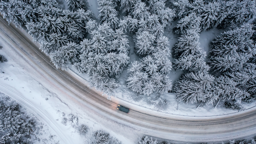 A car on a lonely, snow-filled road in the forest.