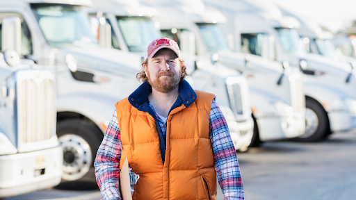 A fleet manager holding a clipboard walks forward with fleet trucks behind him.