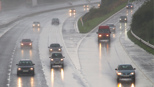 Many cars driving on a highway during a dark and rainy evening.