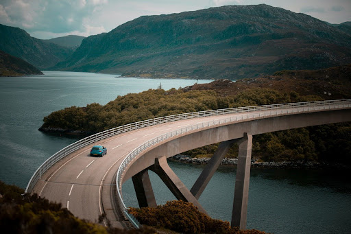 a vehicle driving along a long, curved bridge