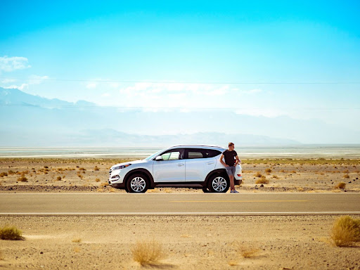 a man leaning on his car on a desert road