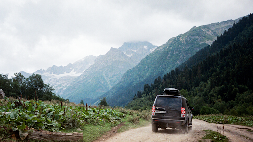 Black SUV driving on a rugged dirt road in the mountains, equipped with all-terrain tires for off-road performance.